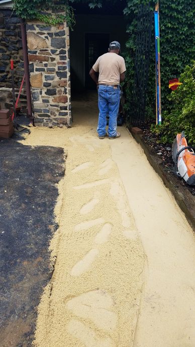 Man standing on a path of light-colored gravel, next to a gravel border. Stone building entrance.