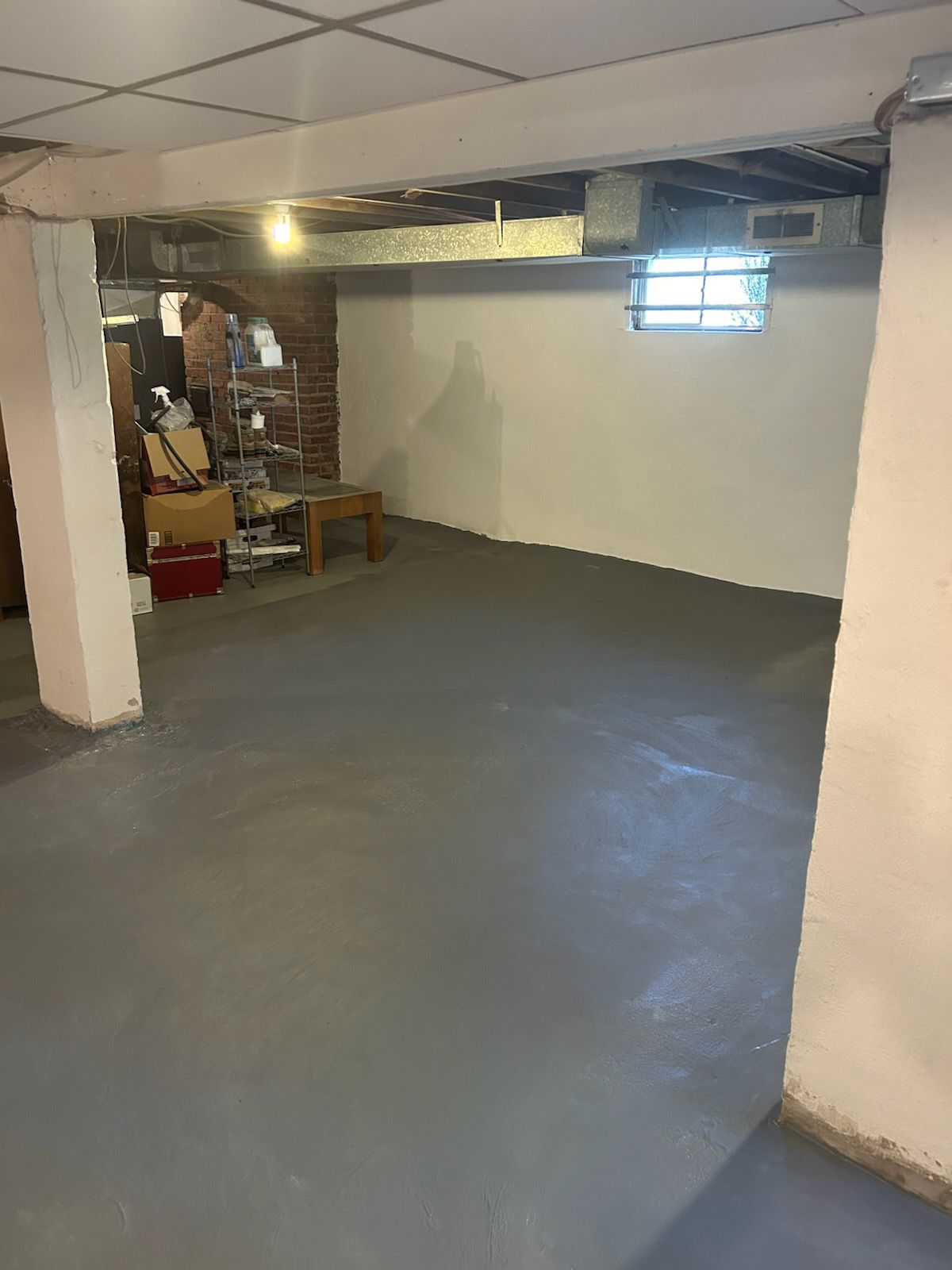 Basement with painted gray floor and white walls, brick accents, and ceiling beams.