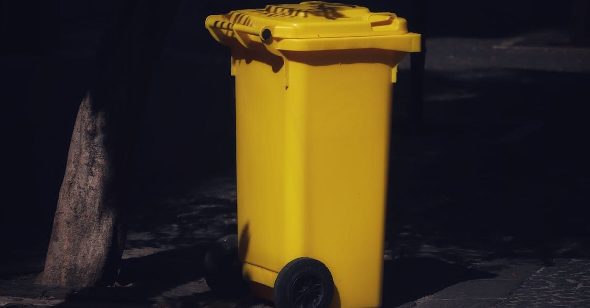 A yellow trash can is sitting on the side of the road at night.