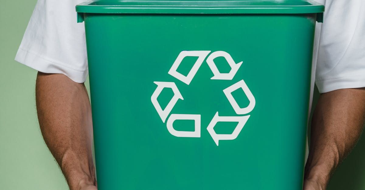 A man is holding a green recycling bin in his hands.