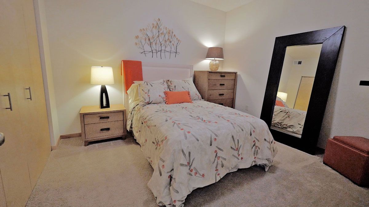 A bedroom with a bed , nightstand , lamp and mirror.
