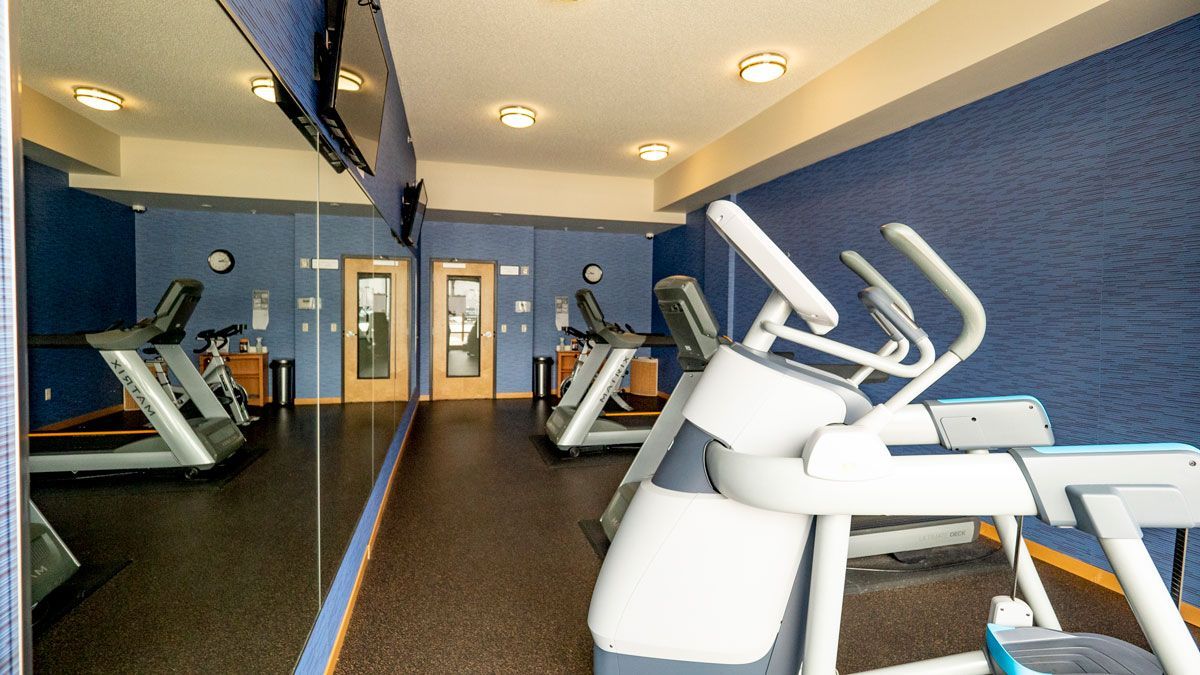 A gym with treadmills and ellipticals in front of a large mirror.