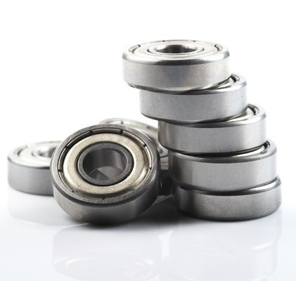 Rodamientos de bolas apilados y dispersos sobre una superficie reflectante blanca.