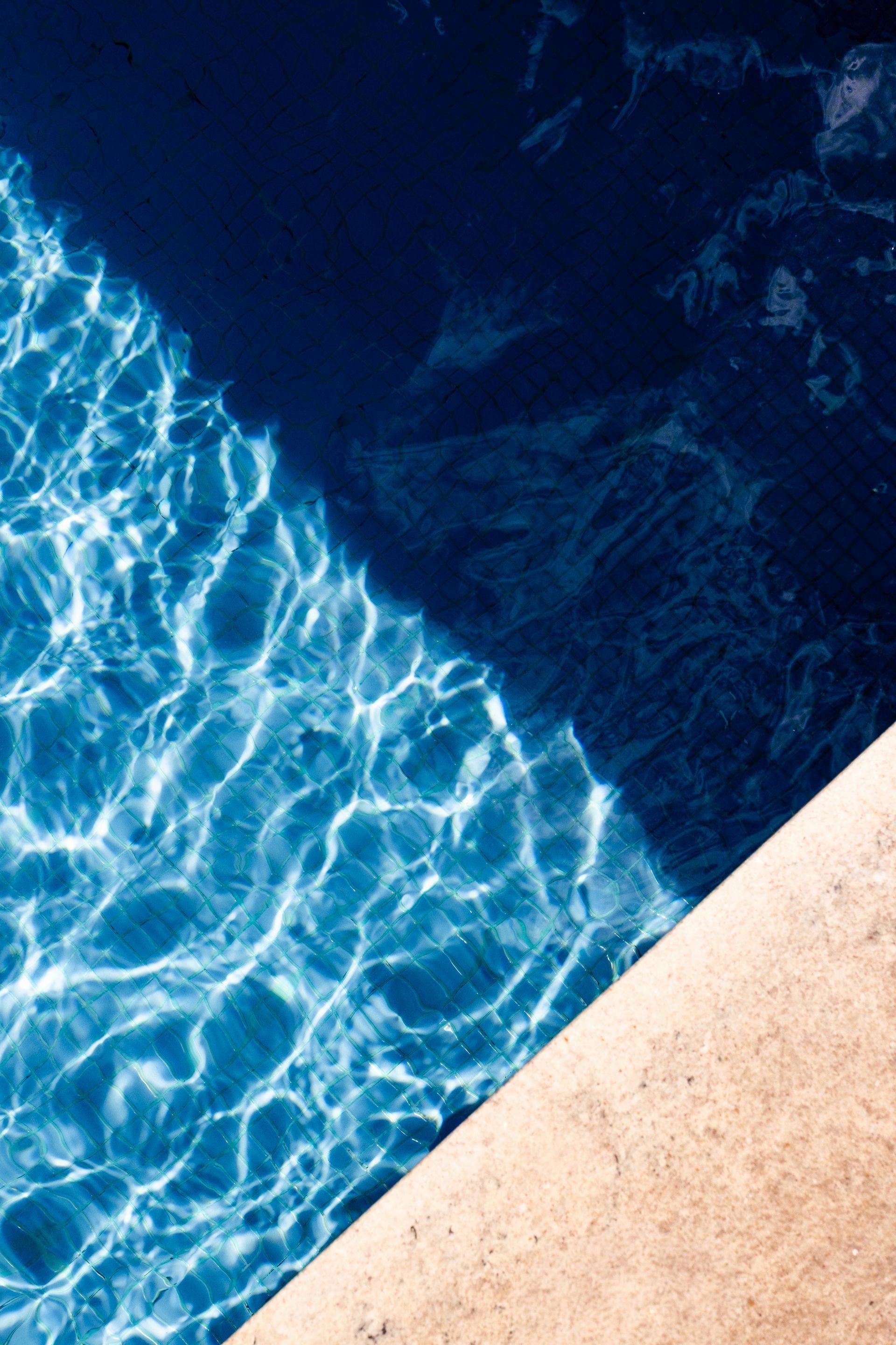 Blue pool water with sunlight ripples beside a beige pool edge