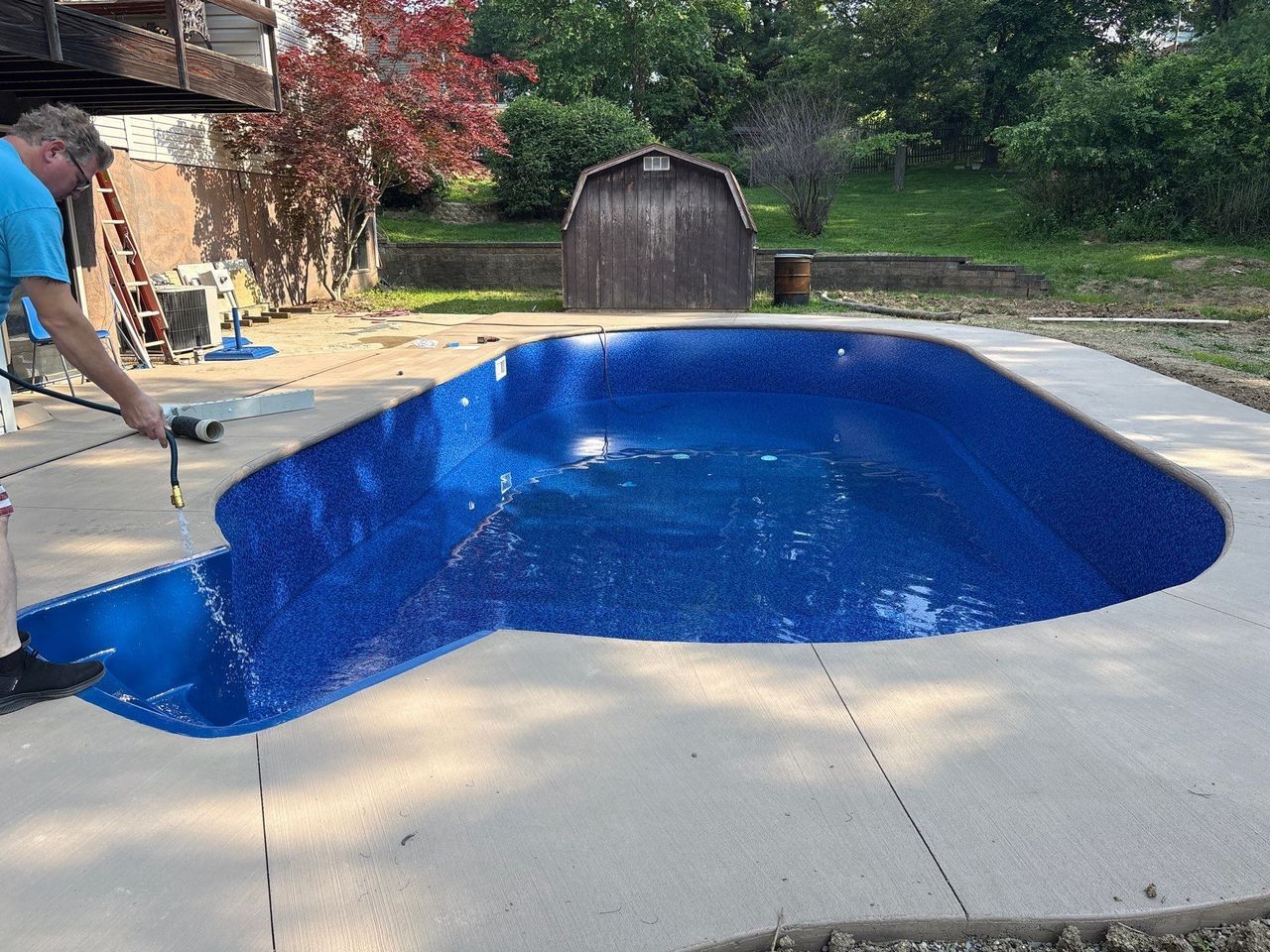 Person using a hose near an empty backyard swimming pool with a damaged edge