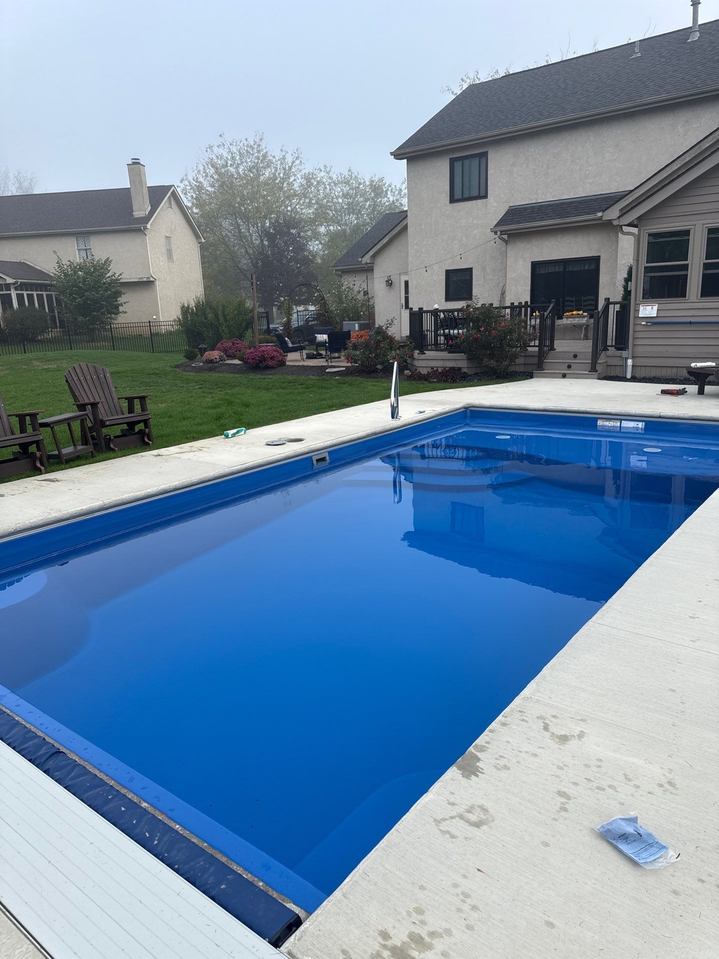 Backyard swimming pool with blue cover beside a house and lawn furniture