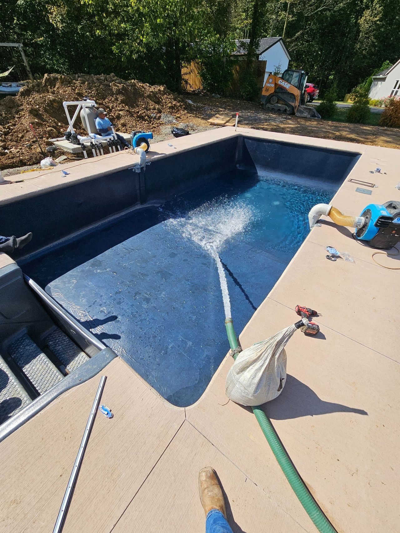 Backyard pool being cleaned with a hose and pool vacuum; cleaning supplies on the deck.