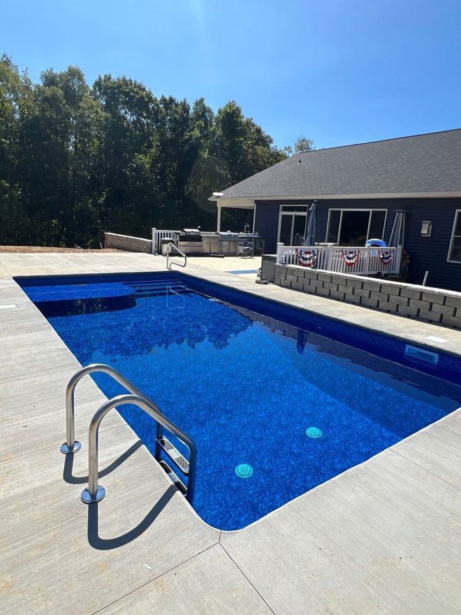 Outdoor swimming pool with blue water beside a house, viewed from a concrete deck under a clear sky