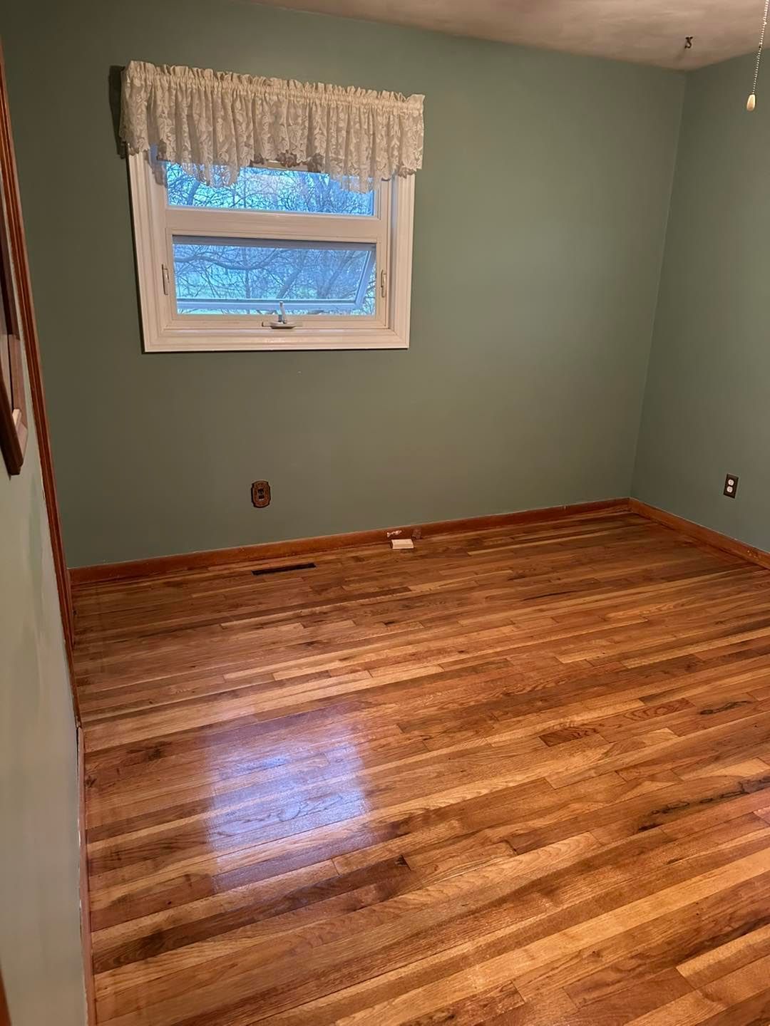 A bedroom with hardwood floors and a window.