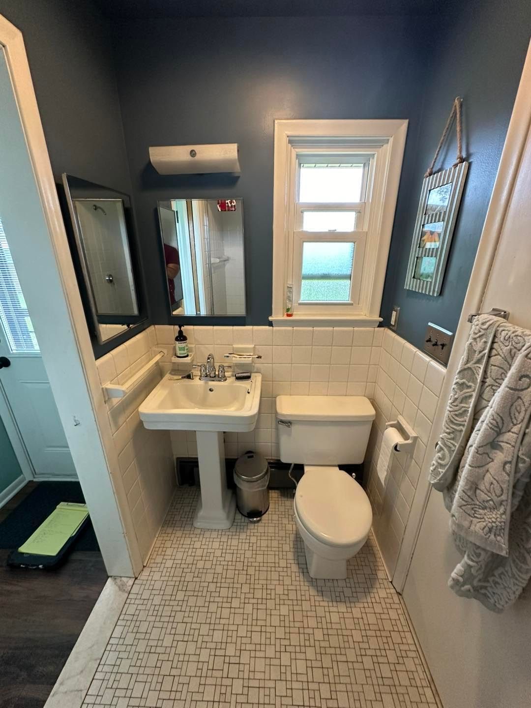 A bathroom with a sink , toilet , mirror and window.