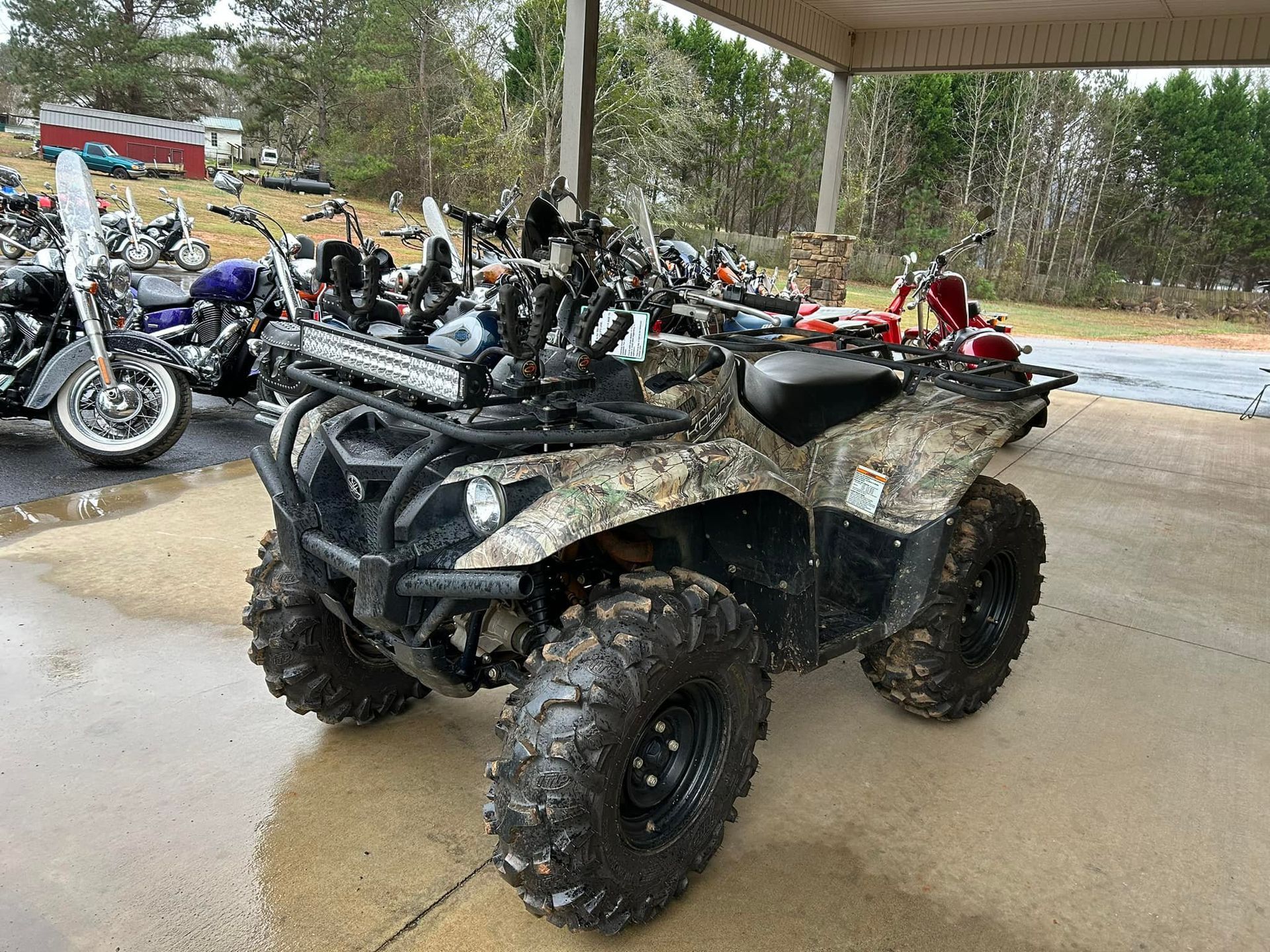 A camouflage atv is parked in a parking lot next to a row of motorcycles.