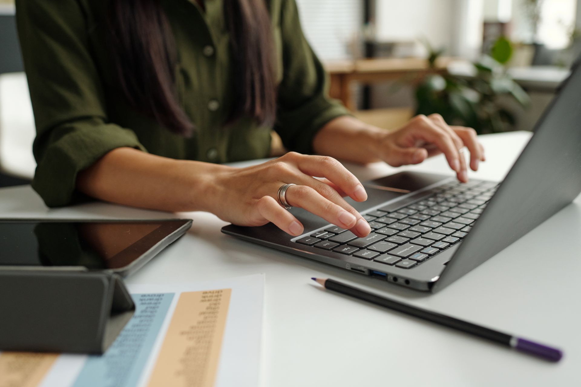 A woman is typing on a laptop computer at a desk.