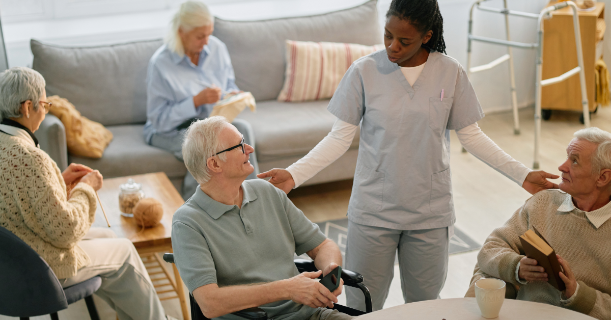 Caregiver in blue scrubs holding hands with an elderly person on a sofa, smiling.