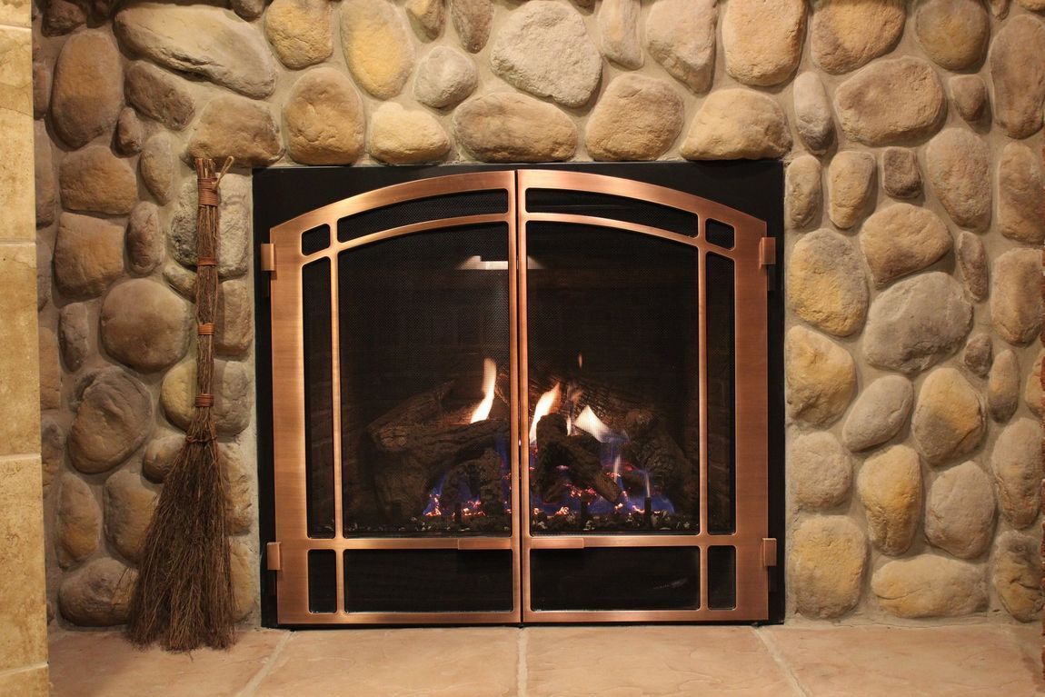 A fireplace with a copper door and a stone wall