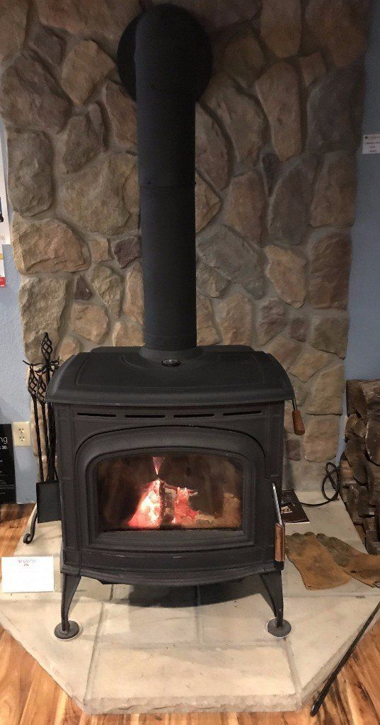 A wood stove is sitting in front of a stone fireplace.