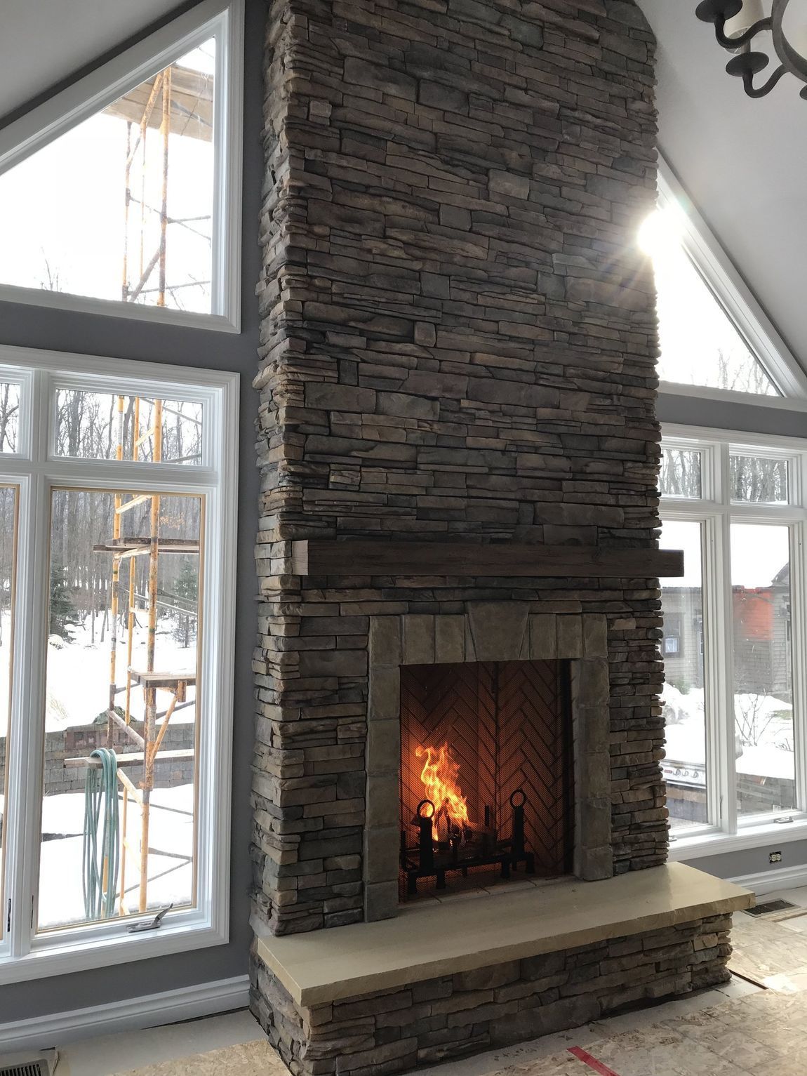 A large stone fireplace in a living room with lots of windows.