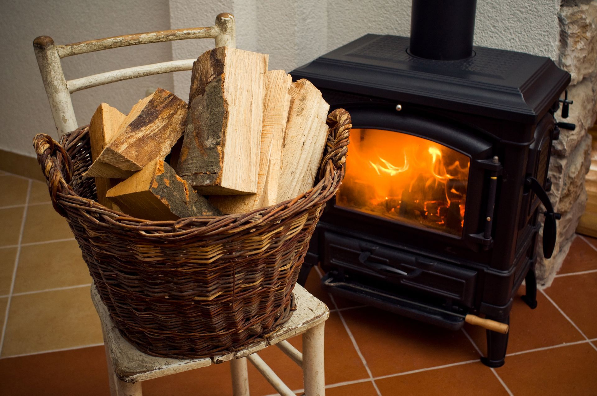 A basket of logs is sitting on a chair next to a wood stove.