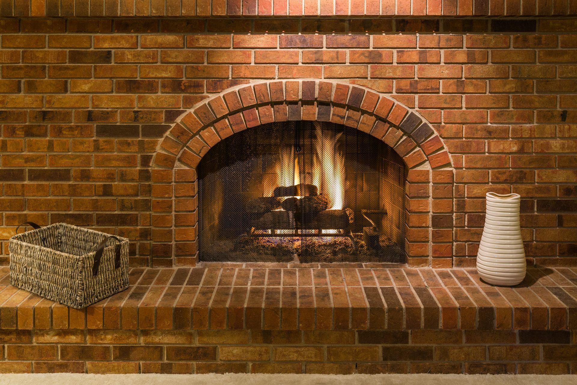 A brick fireplace with a basket and vase on the mantle.