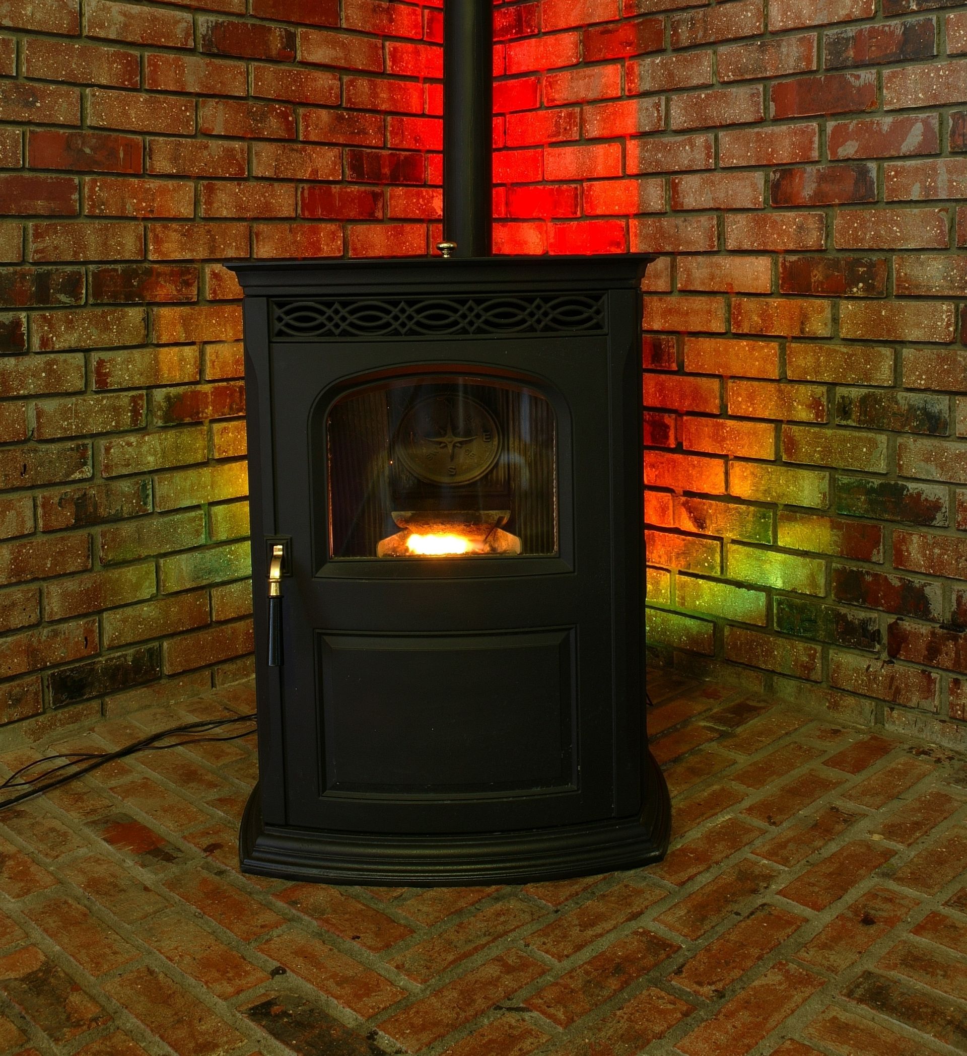 A wood stove is sitting in the corner of a room with a brick wall.
