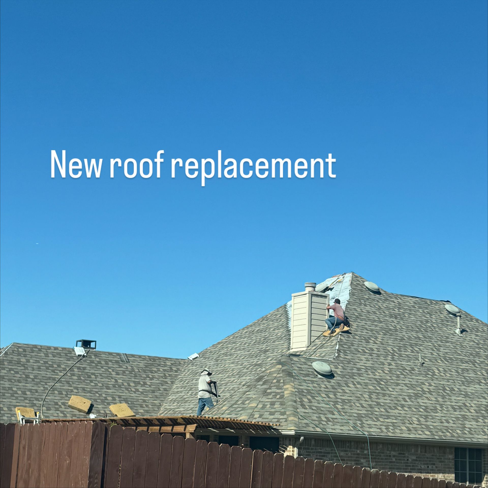 Roofers replacing a roof on a house under a clear, blue sky.