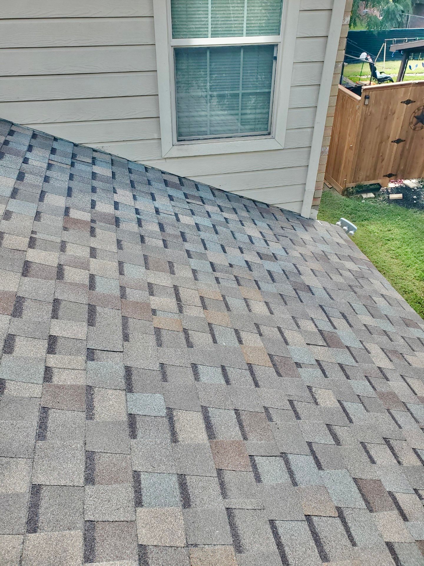 Close-up of a roof covered in gray and brown shingles; a white-framed window is above the roof.