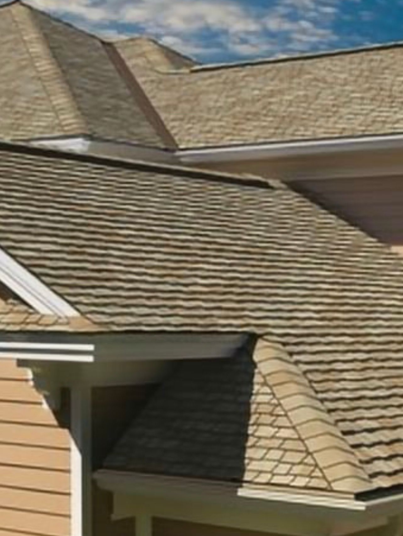 Tan shingled roof of a house against a blue sky, with white trim.