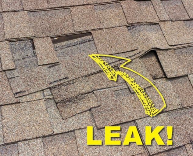 Close-up of damaged asphalt shingles with missing pieces and a drawn arrow pointing at the 