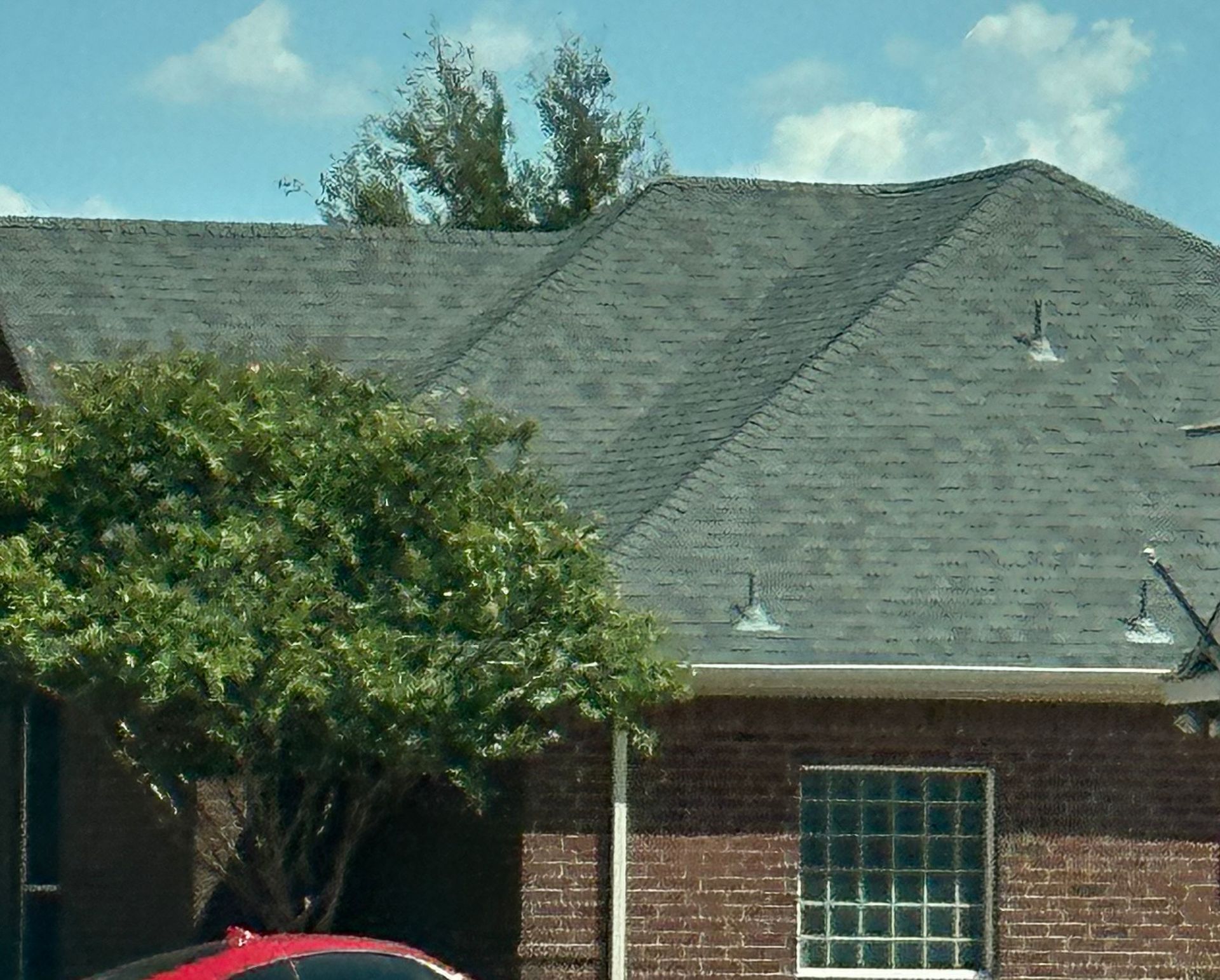 Red brick home with gray shingled roof, glass block window, and a green leafy tree.