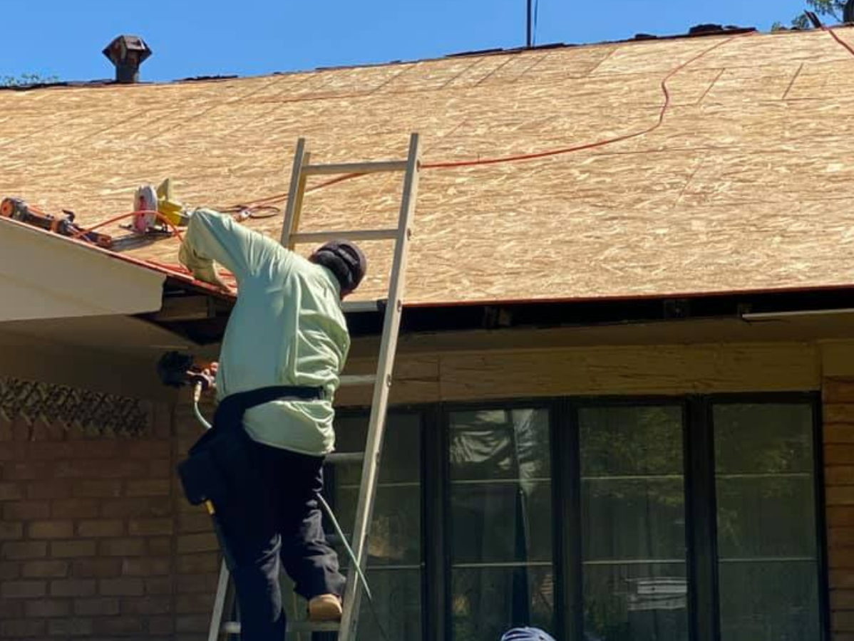 Person on a ladder working on a roof, securing something.