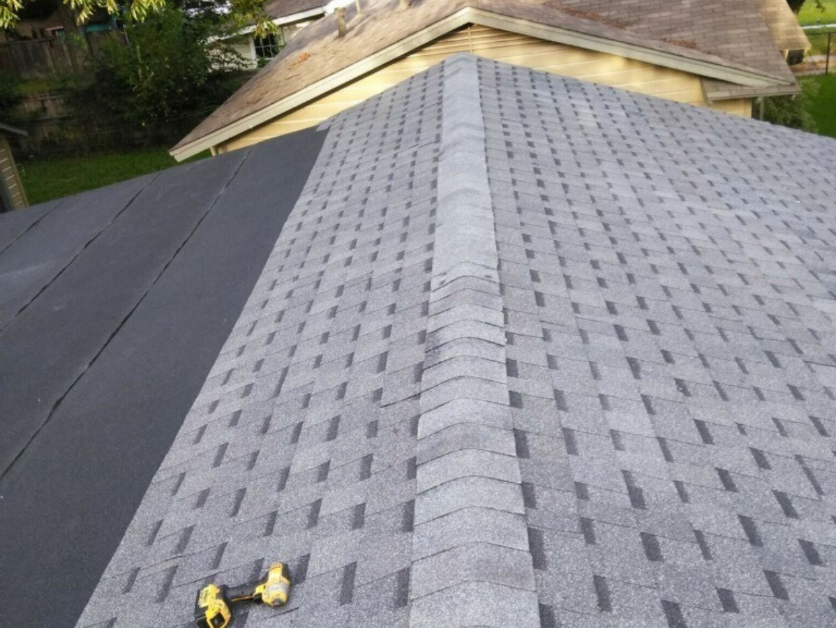 Newly installed gray asphalt shingle roof, with a black section and a central ridge, and a screwdriver.