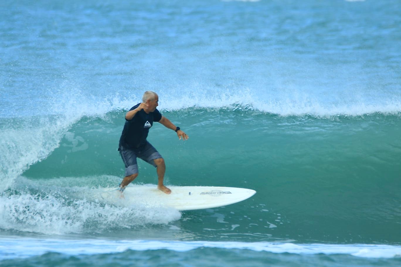 Man surfing a turquoise wave, blue ocean, gray sky.