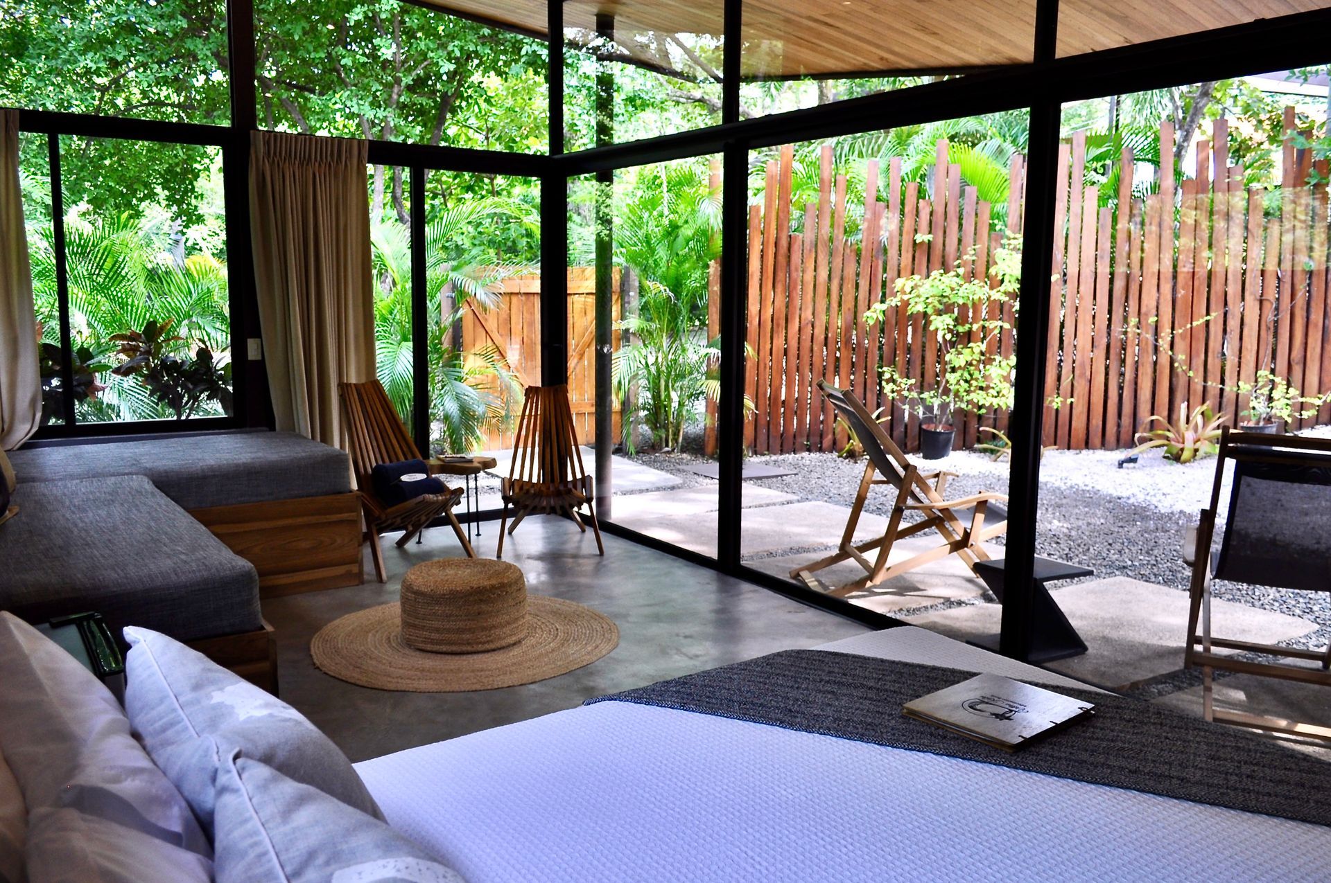 Bedroom with large windows overlooking a lush garden. Furnishings include a bed, seating, and a woven rug.