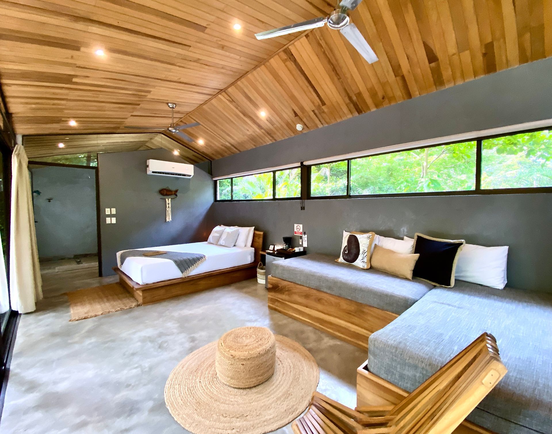 Bedroom with gray walls, wooden ceiling, bed, and couch. Wide brim hat on the floor.