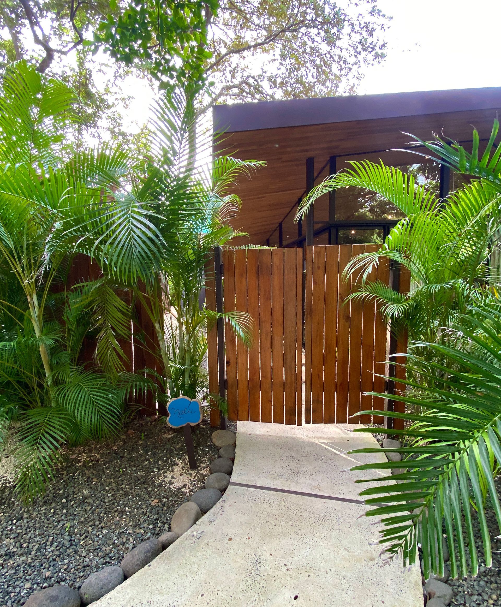 Wooden gate leads to building, surrounded by lush green plants and stone walkway.