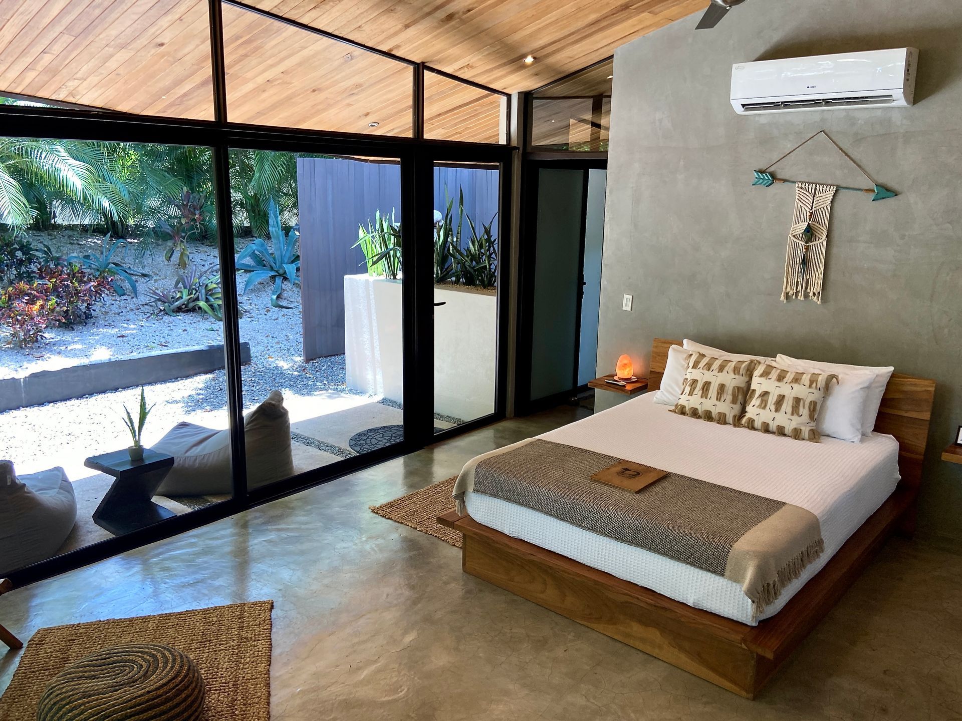 Bedroom with floor-to-ceiling windows, bed, woven rug, and view of patio seating area.