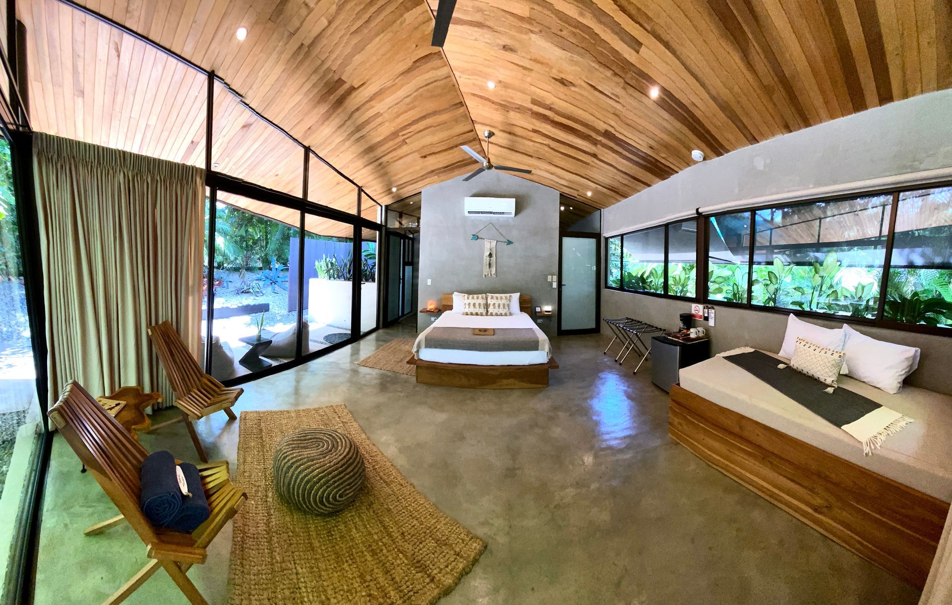 A modern bedroom with wooden ceiling, large windows, and comfortable seating.