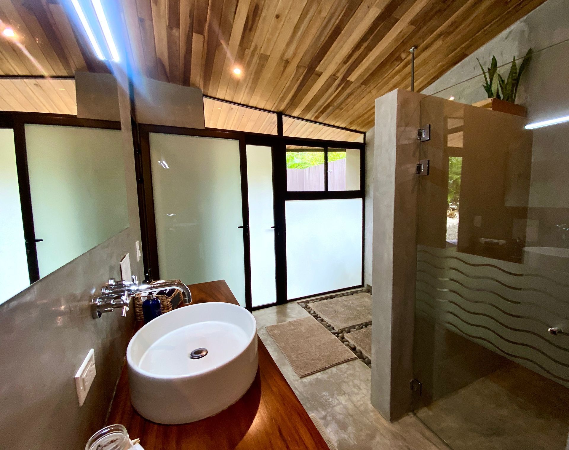 Bathroom with wooden ceiling, oval sink, glass shower, and frosted glass door.