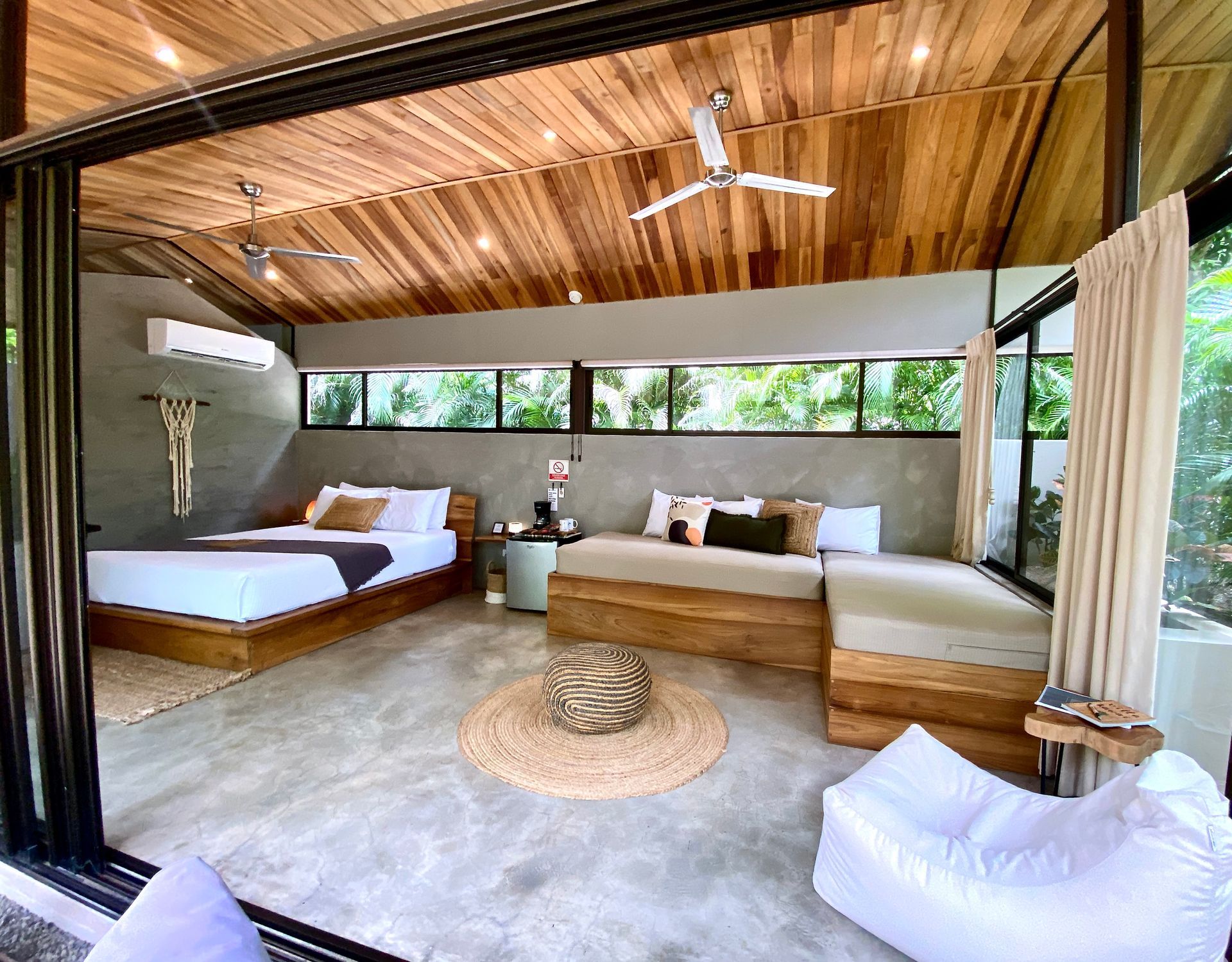 Bedroom with wooden ceiling, bed, sofa, beanbag, and open doors to greenery.