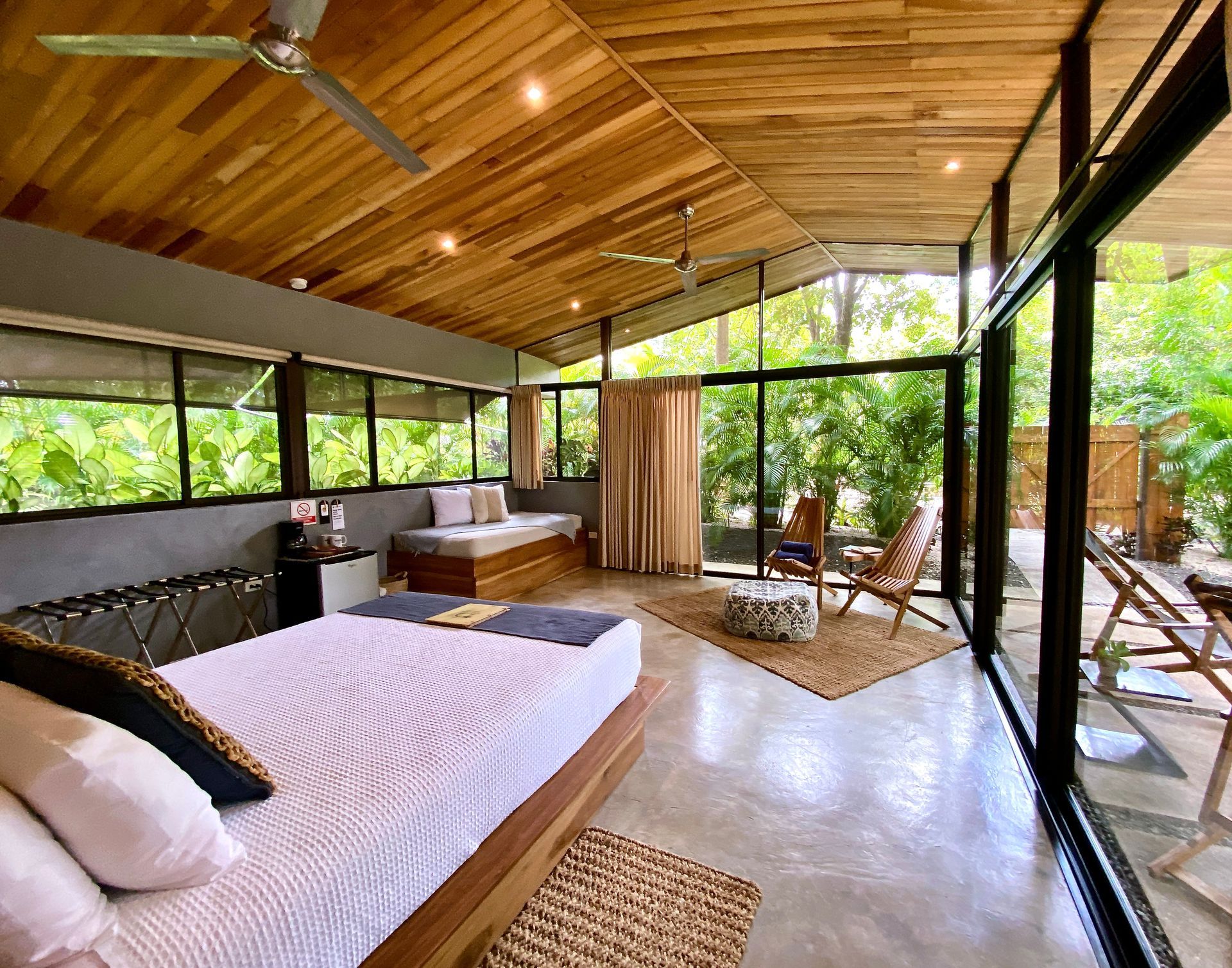 Bedroom with wood ceiling, large windows, bed, seating area, and outdoor patio.