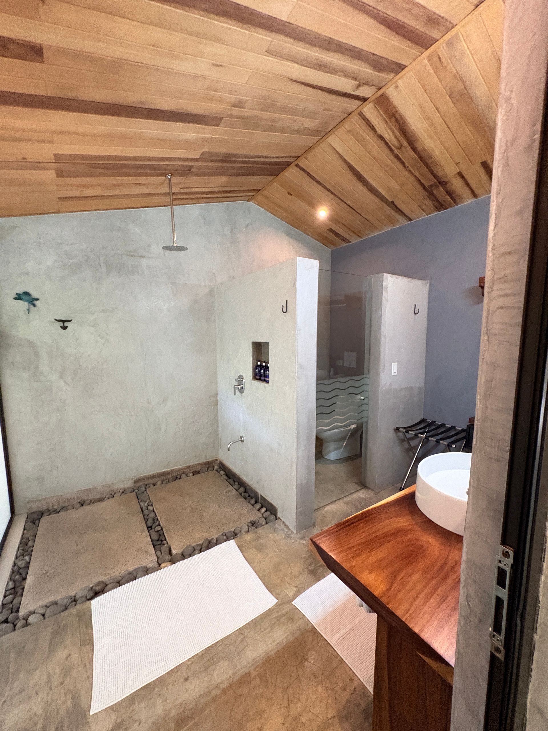 Rustic bathroom with stone shower floor, wooden ceiling, and sink on a wooden cabinet.