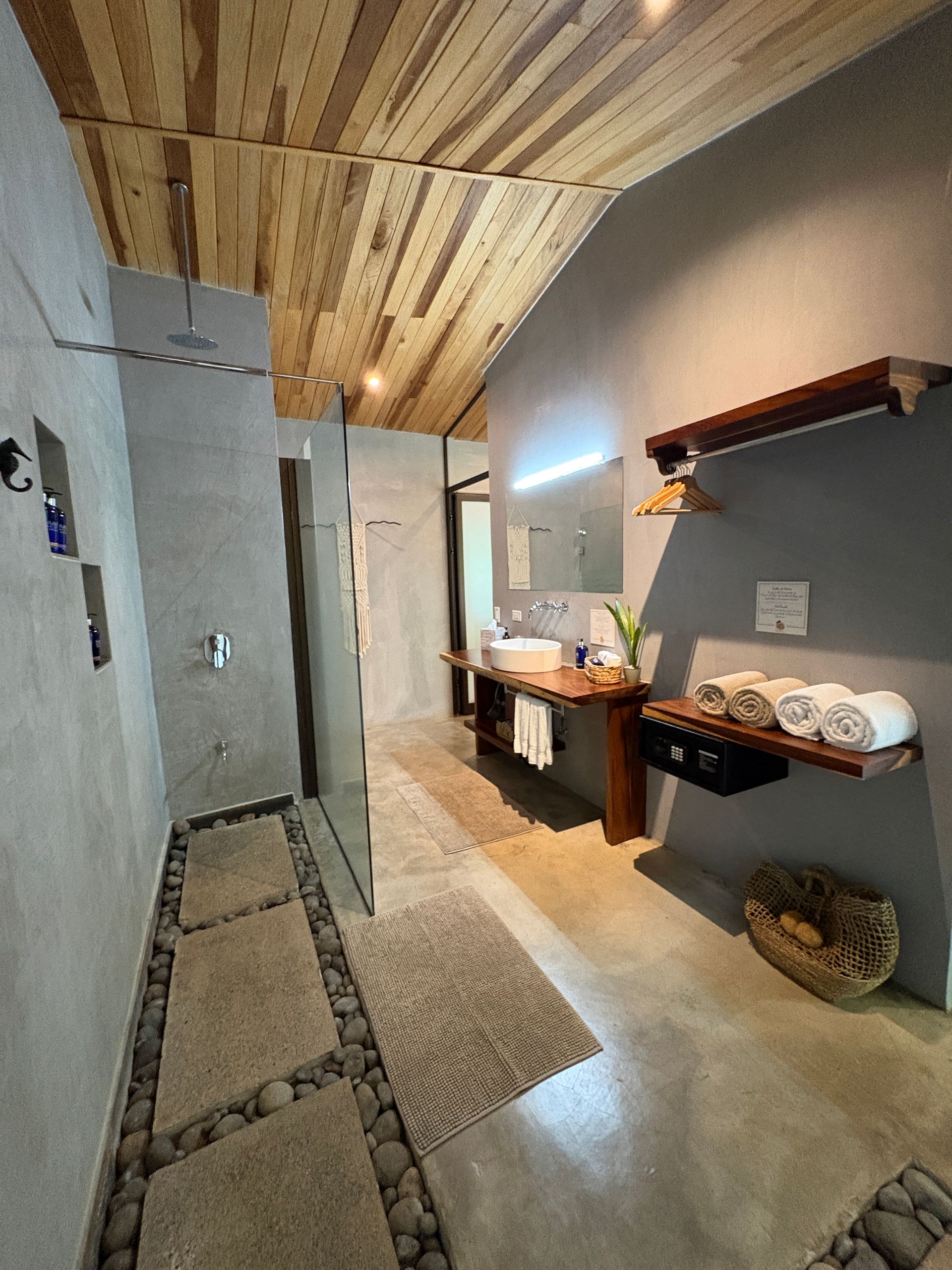 Bathroom with gray walls, wood ceiling, stone shower floor, wood vanity, and stacked towels.