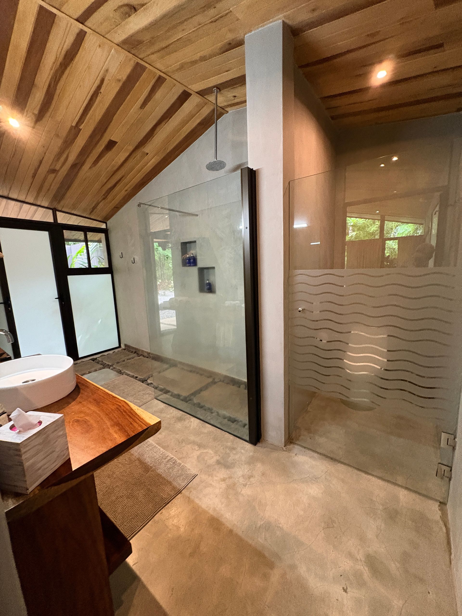Bathroom with wood ceiling, concrete floor, glass shower, and wooden vanity.