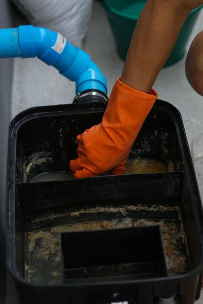 Person in orange glove cleaning a black container with blue pipe attached, likely part of a filter.