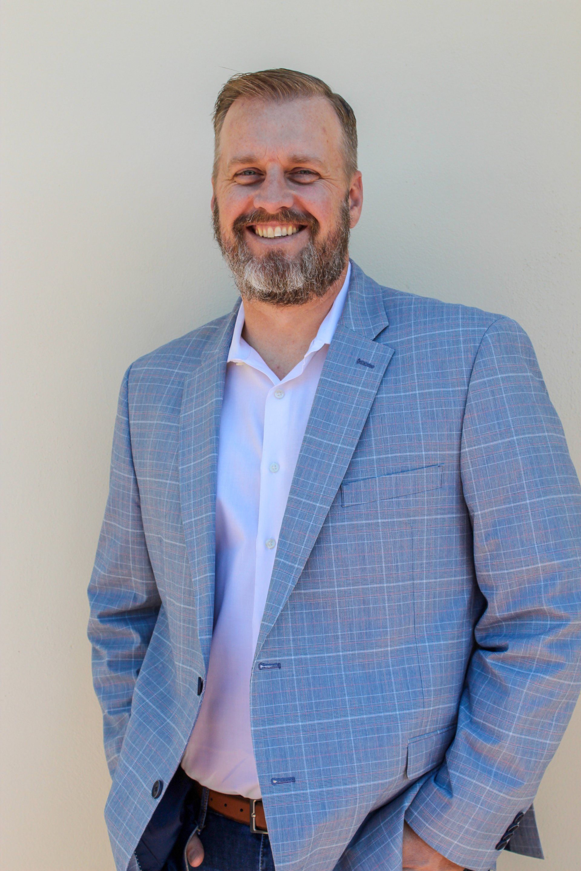 A man with a beard is wearing a blue jacket and a white shirt.