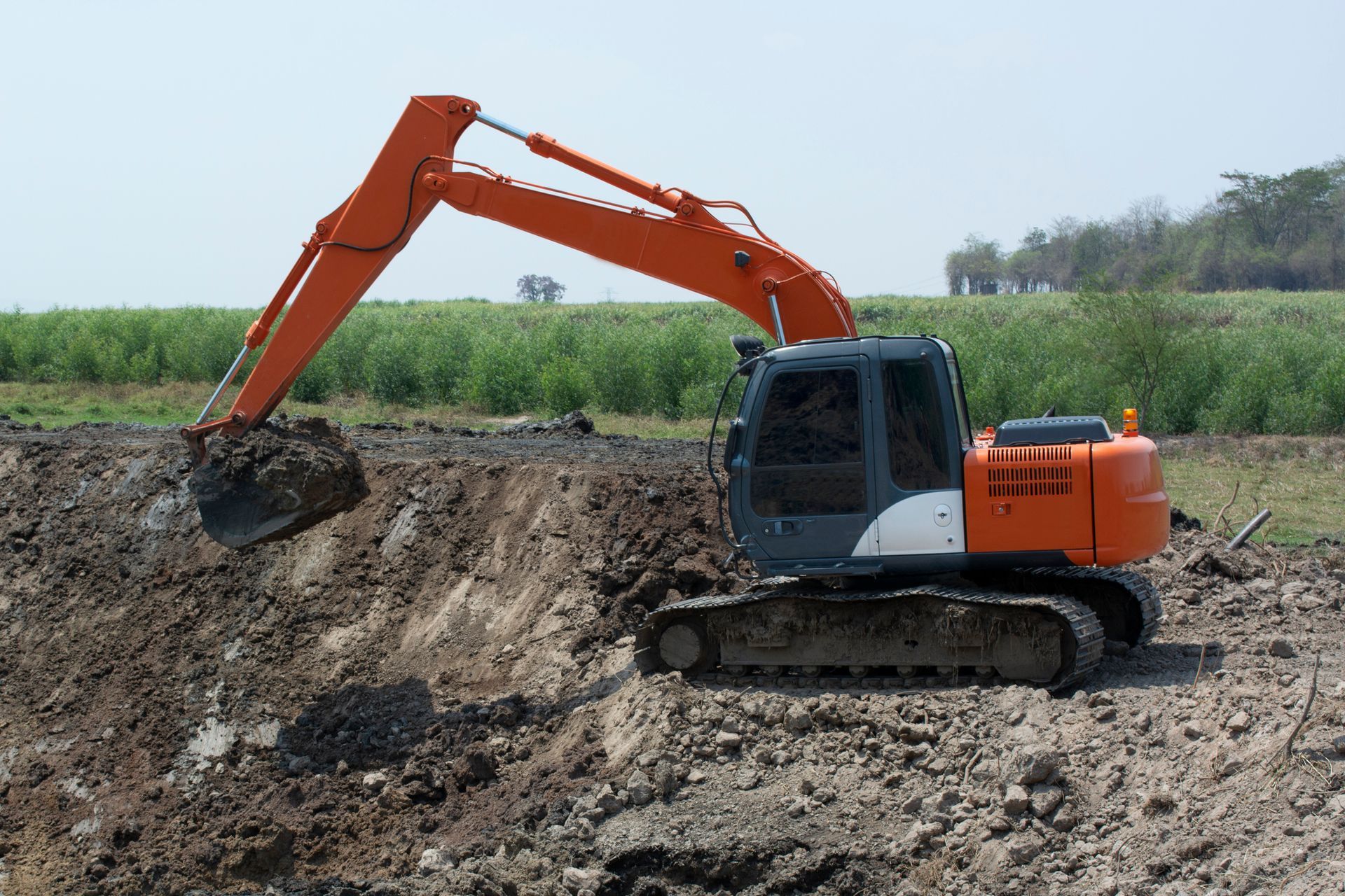 Orange excavator digging earth in a field.