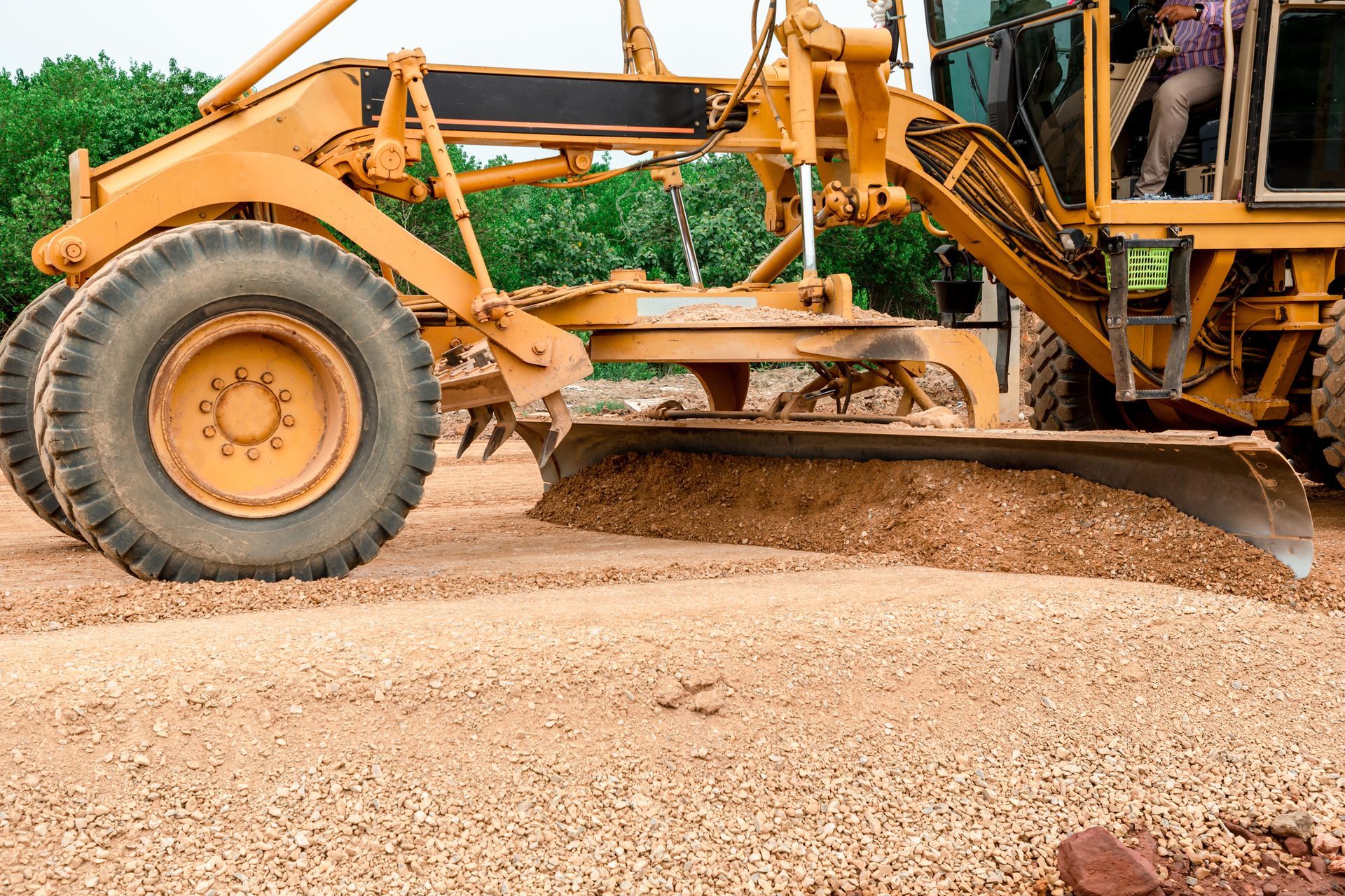 Yellow motor grader smoothing gravel road surface.