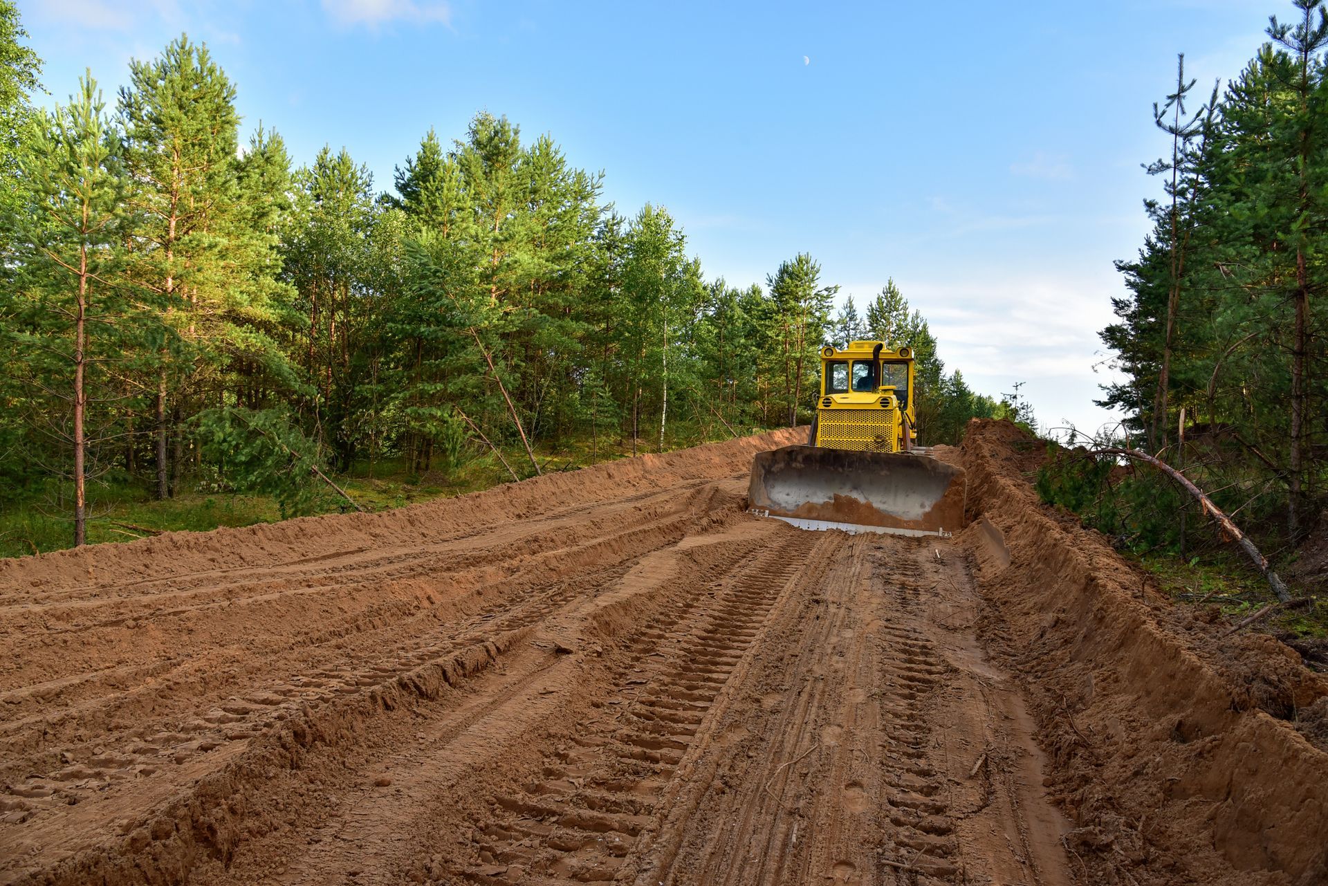 Yellow bulldozer clearing a dirt path in a forest.