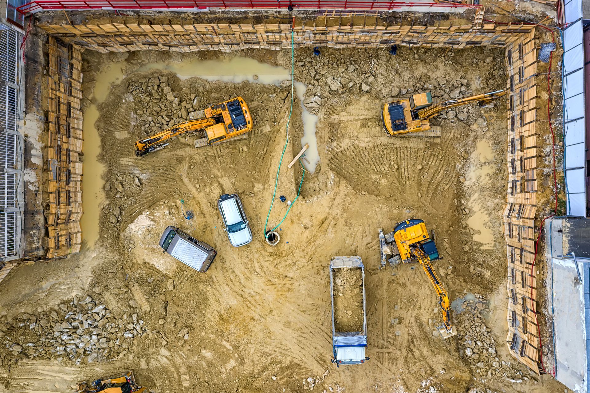 Aerial view of a construction site with excavators, dump trucks, and a deep, open pit surrounded by wooden walls.