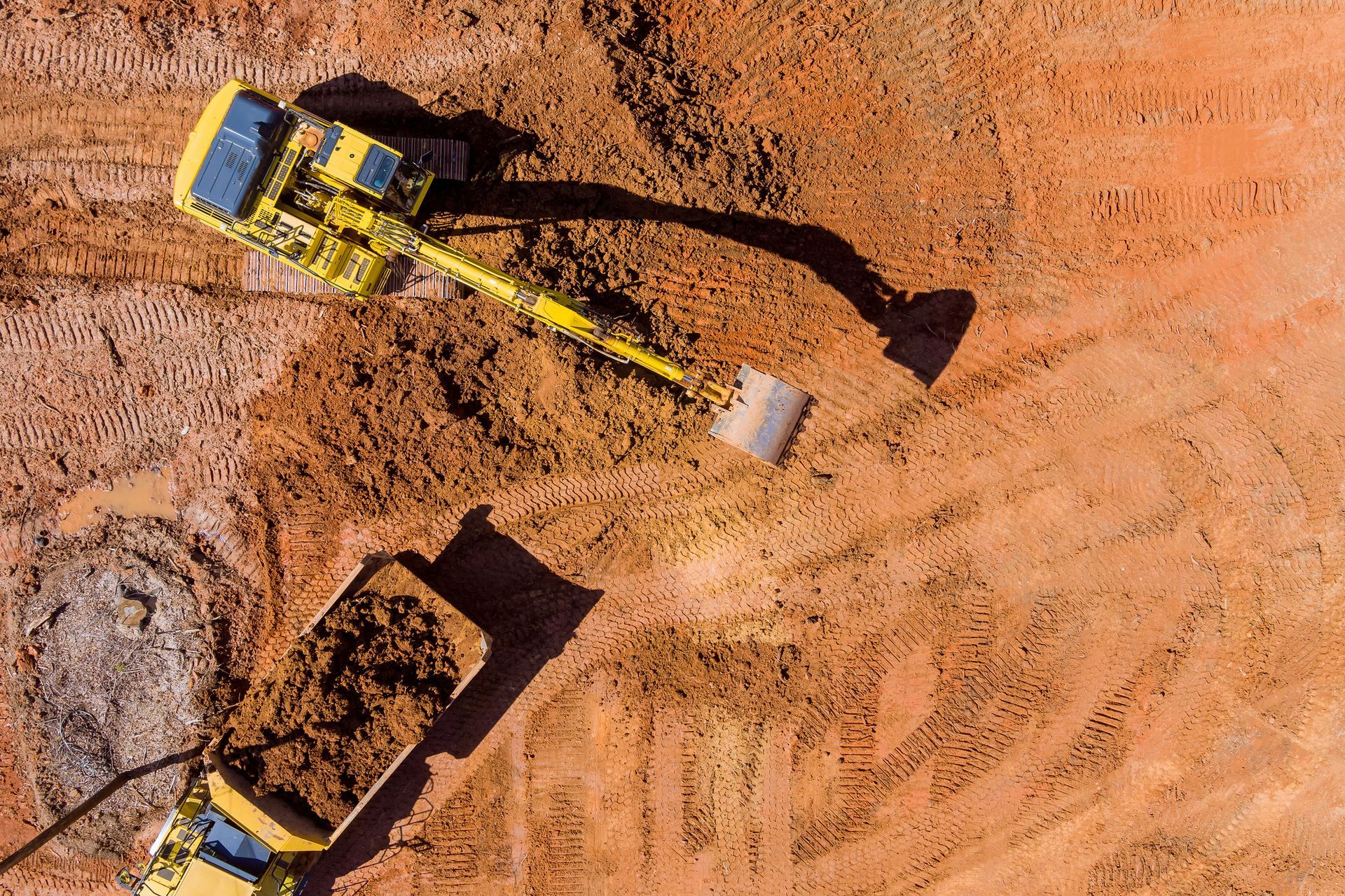 Yellow excavator loading dirt into a dump truck on reddish-brown earth.