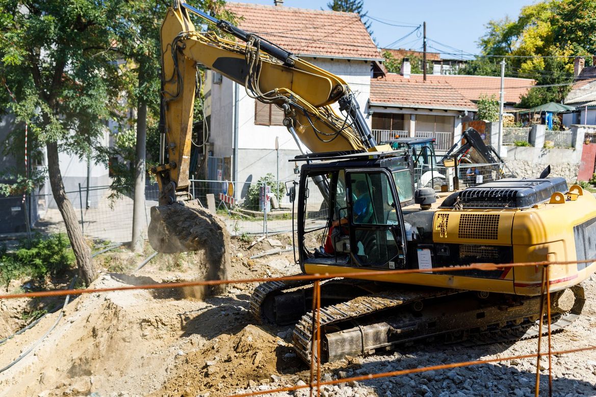 Yellow excavator digging in a construction site with houses in the background.